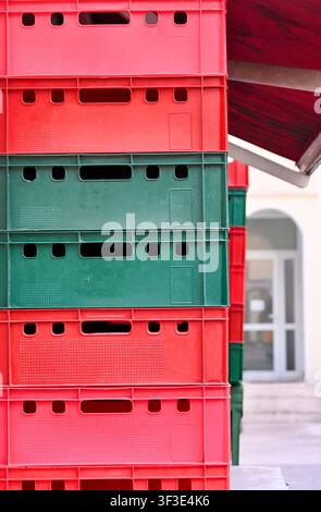 Front view close-up of colorful red and green plastic storage crates stacked vertically on top of each other. Bright geometric texture and pattern suitable for logistics, warehousing, transport, agriculture, recycling, container organization, and supply chain concepts. Stock Photo