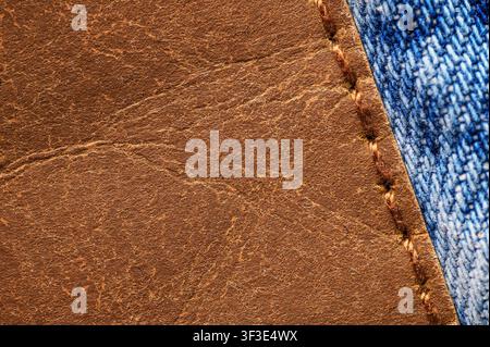 Close-up of brown leather patch stitched onto blue denim fabric. Stock Photo