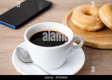 Black coffee with glazed donuts and smartphone on wooden table Stock Photo