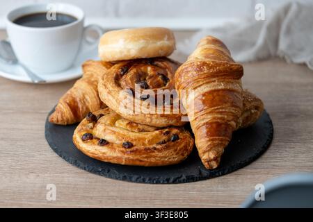 Assorted breakfast pastries with black coffee on wooden table Stock Photo
