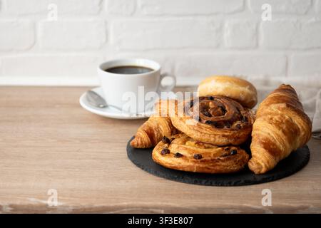 Assorted breakfast pastries with black coffee on wooden table Stock Photo