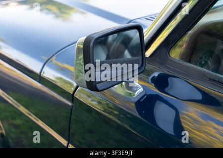 Close-up of a vintage car's driver-side mirror with a rectangular black frame on a glossy dark blue exterior Stock Photo