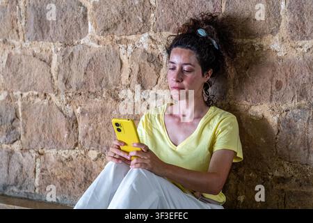 Woman using smartphone by stone wall relaxing Stock Photo