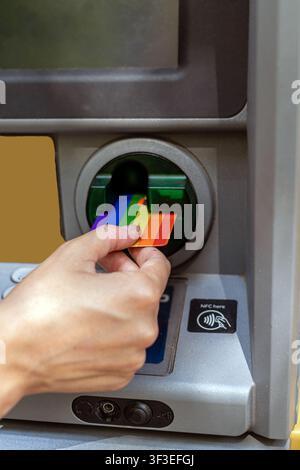 Hand inserting rainbow credit card into an atm Stock Photo