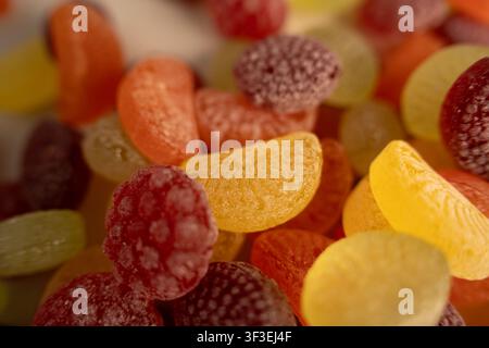 macro closeup of colorful sugared fruit flavored gummy candies and soft jelly slices piled together on a tabletop, warm saturated yellows, oranges, re Stock Photo