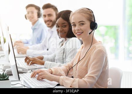 Group of call centre employees smiling and working on computers at light office, copy space Stock Photo