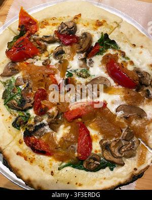 A close-up of a slice of pizza with red peppers, mushrooms, spinach, onion, and white cheese, no red sauce pizza. Stock Photo