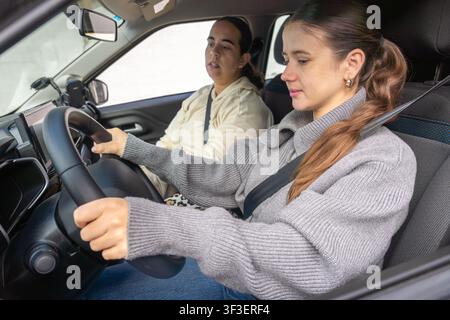Close-up of student driver's hands firmly holding steering wheel, driving instructor visible in background, car interior, learning to drive concept Stock Photo