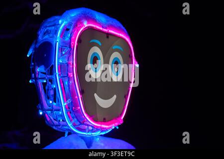 A close-up photograph of a robotic head illuminated by vibrant neon pink and blue LED lights against a completely dark black background. The robot Stock Photo