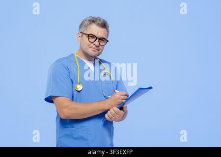 A professional doctor wearing scrubs and a stethoscope, attentively taking notes on a clipboard during a medical appointment. Stock Photo