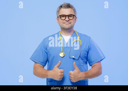 A confident doctor in blue scrubs and glasses gives a thumbs up, symbolizing positive patient experiences and modern healthcare practices. Stock Photo