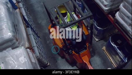 Forklift driver driving warehouse aisle, adjusting levers and activating network around operator Stock Photo