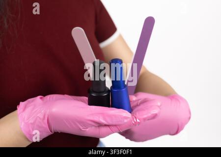 Manicurist hands in pink gloves holding color nail files and polish Stock Photo