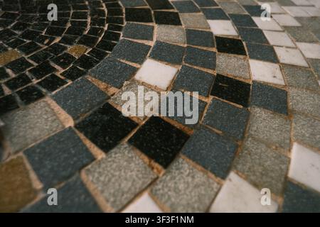 Close-up of a textured circular mosaic tile surface featuring black, white, and grey squares with visible rough grout lines and shallow depth of field Stock Photo