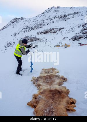 Man drilling a hole to ice fish near Honningsvag Stock Photo