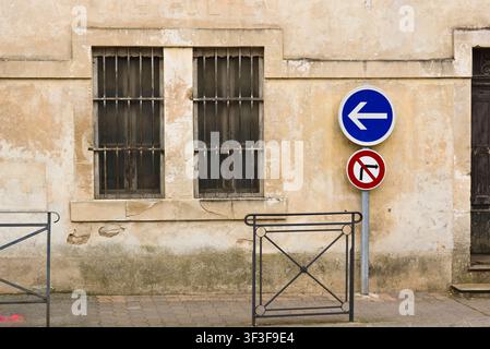 French road traffic signs next to grated windows on a weathered building facade in Fonvieille, Provence, France. Stock Photo
