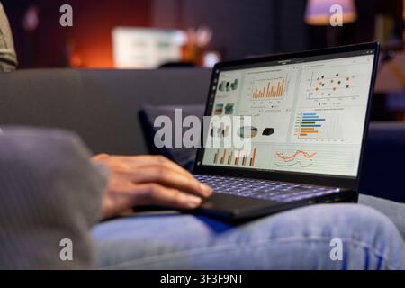 Black focused specialist working from home using financial graphs analysis, reviewing statistical data to compare supply and demand numbers. Examining business charts on his laptop. Stock Photo