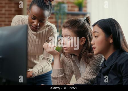 Software engineer points at a computer screen while explaining running code to coworkers, brainstorming software ideas and collaborating on an IT group project. Stock Photo