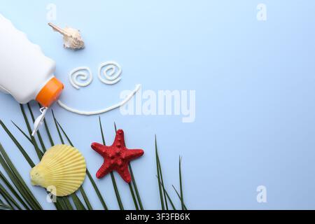 Smiling face made with sunscreen, bottle of sun protection product, seashells and leaves on light blue background, flat lay. Space for text Stock Photo