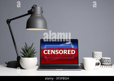 Laptop displaying censored content on desk. Information filtering Stock Photo