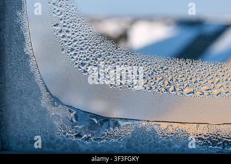 Macro close-up early morning frost and melting ice droplet on window glass with blurred sunrise background Stock Photo