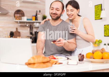 Couple talking online with family on a video call during breakfast, videoconference in the morning, using online web internet technology, talking and communicating with relatives. Stock Photo