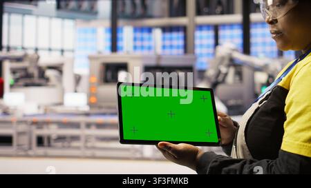Smart factory specialist using green screen tablet to test automated systems to ensure reliability. Industry 4.0 plant technician using chroma key device to identify bottlenecks and optimize, camera A Stock Photo