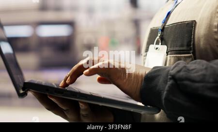 Industrial plant expert overseeing installation process using laptop, troubleshooting errors. Manufacturing facility employee calibrating automated robotic arms using notebook, camera B closeup Stock Photo