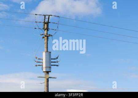 Pole mounted distribution transformer on a wooden electricity pole against blue sky Stock Photo
