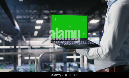 Close up of data center admins on industrial platform using green screen laptop, collaborating on tasks. Server hub workers visualizing large language model architecture using chroma key notebook Stock Photo