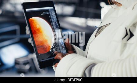 Astronaut inside futuristic spaceship checking red planet journey analytics during routine mission check. Space station cosmonaut using device, standing near monitor showing Mars expedition metrics Stock Photo