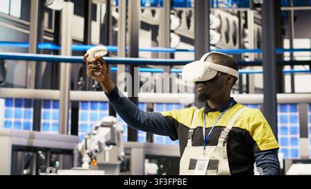 Smart factory specialist using virtual reality simulation to predict equipment failures. Industry 4.0 plant engineer using VR headset to follow maintenance procedures and repair damages, camera B Stock Photo