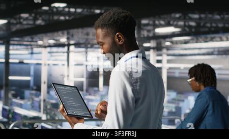 Data center programmers on industrial platform checking lines of code, collaborating on tasks. Server hub IT specialists visualizing large language model architecture using tablet and PC Stock Photo