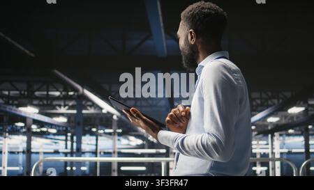 Engineer walking on data center industrial platform, performing system maintenance. IT professional using tablet to do upgrades, resolving bugs and enhancing infrastructure stability, Stock Photo