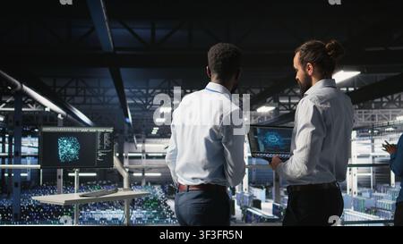 Data center workers cooperating, doing maintenance on rigs handling AI processing tasks. Server hub admins doing brainstorming, managing storage arrays supporting deep learning technology, Stock Photo
