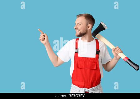 Smiling young man in red overalls holding an axe and pointing to the side, Construction and handyman Stock Photo