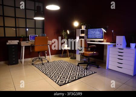 Modern home office interior with two computer workstations and coding on screens at night Stock Photo