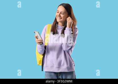 Smiling young woman student with backpack and wired earphones listening to music on smartphone Stock Photo