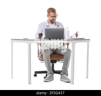Smiling young man in glasses working on a laptop at a modern desk with documents and coffee isolated on white background Stock Photo