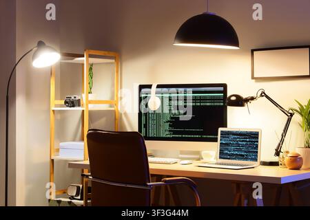 Home office workspace with computer monitor and laptop displaying code at night, remote work and programming Stock Photo