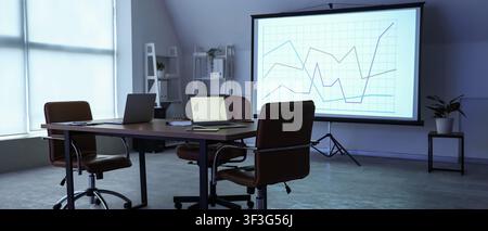 Empty modern conference room with laptops on a table and a projection screen displaying a business graph, an empty modern conference room features a l Stock Photo