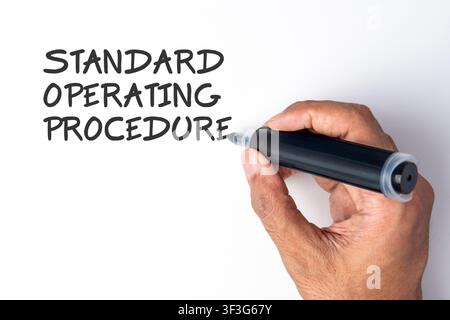 Hand holding a black marker writing the phrase Standard Operating Procedure on a white background. Corporate guidelines, business workflows Stock Photo