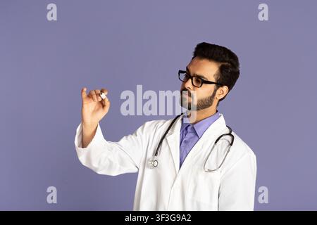 Serious Indian doctor writing with marker on virtual screen against lilac background, space for design Stock Photo