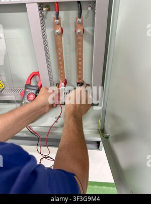 Electrical technician using a digital multimeter to measure voltage inside an industrial electrical control panel during maintenance and inspection in Stock Photo