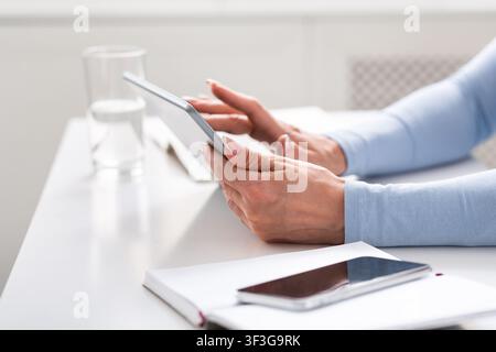 Using mobile devices at home and workplace. Adult female hands work on digital tablet on white table Stock Photo