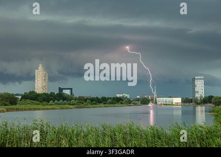 View of a lightning strike hitting near modern buildings and a lake in Latvia. Stock Photo