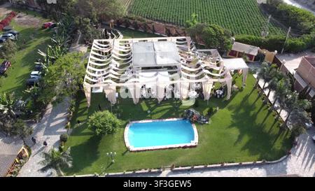 Aerial view of a wedding reception setup in a lush garden with a swimming pool, elegant white tent, and dining tables arranged on the lawn in Lima, Li Stock Photo