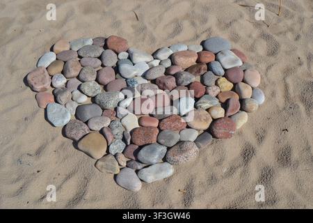 A charming heart shape formed by an arrangement of multicolored beach pebbles and stones on golden sand Stock Photo