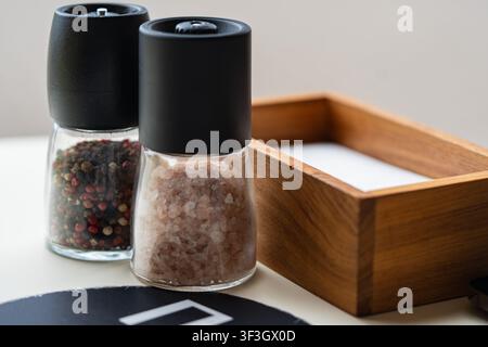 Himalayan pink salt and mixed pepper in glass grinders on restaurant table Stock Photo