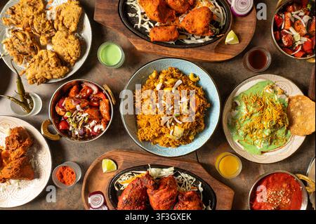 Indian food feast featuring assorted traditional dishes including biryani, tandoori chicken, fried chicken, curries, rice, sauces and vegetable sides Stock Photo